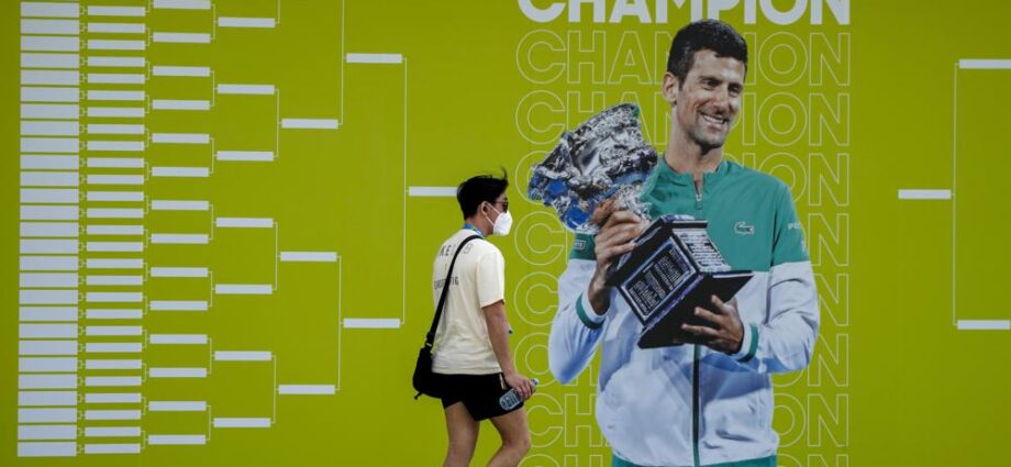 Un hombre camina junto a un anuncio del Abierto de Australia, en el que aparece Novak Djokovic, el martes 11 de enero de 2022, en Melbourne (AP Foto/Mark Baker)